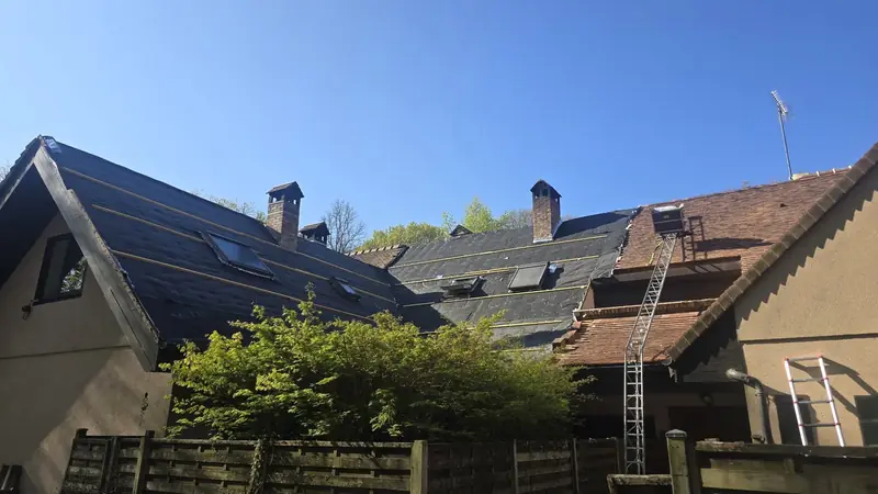 Pan de toiture recouvert de son écran de sous-toiture noir à côté d'un pan encore couvert de tuiles anciennes