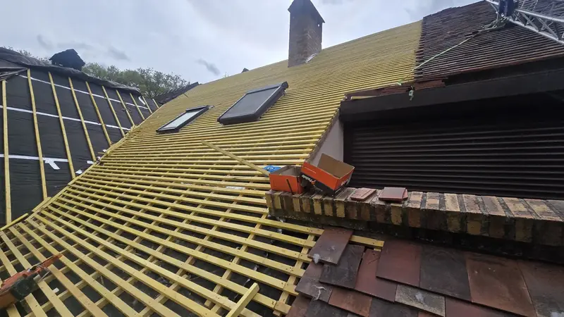 Liteaux neufs autour d'une fenêtre de toit, tuiles anciennes stockées au bord du toit, Chevreuse (78)