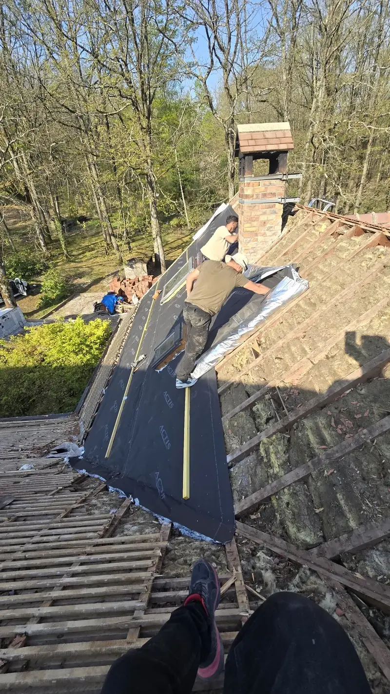 Couvreurs déroulant l'écran de sous-toiture sur la charpente après dépose des tuiles, Chevreuse (78)