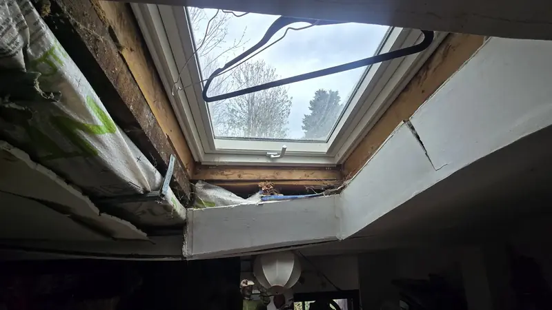 Fenêtre de toit vue de l'intérieur avant travaux, habillage décollé et traces d'infiltration au plafond