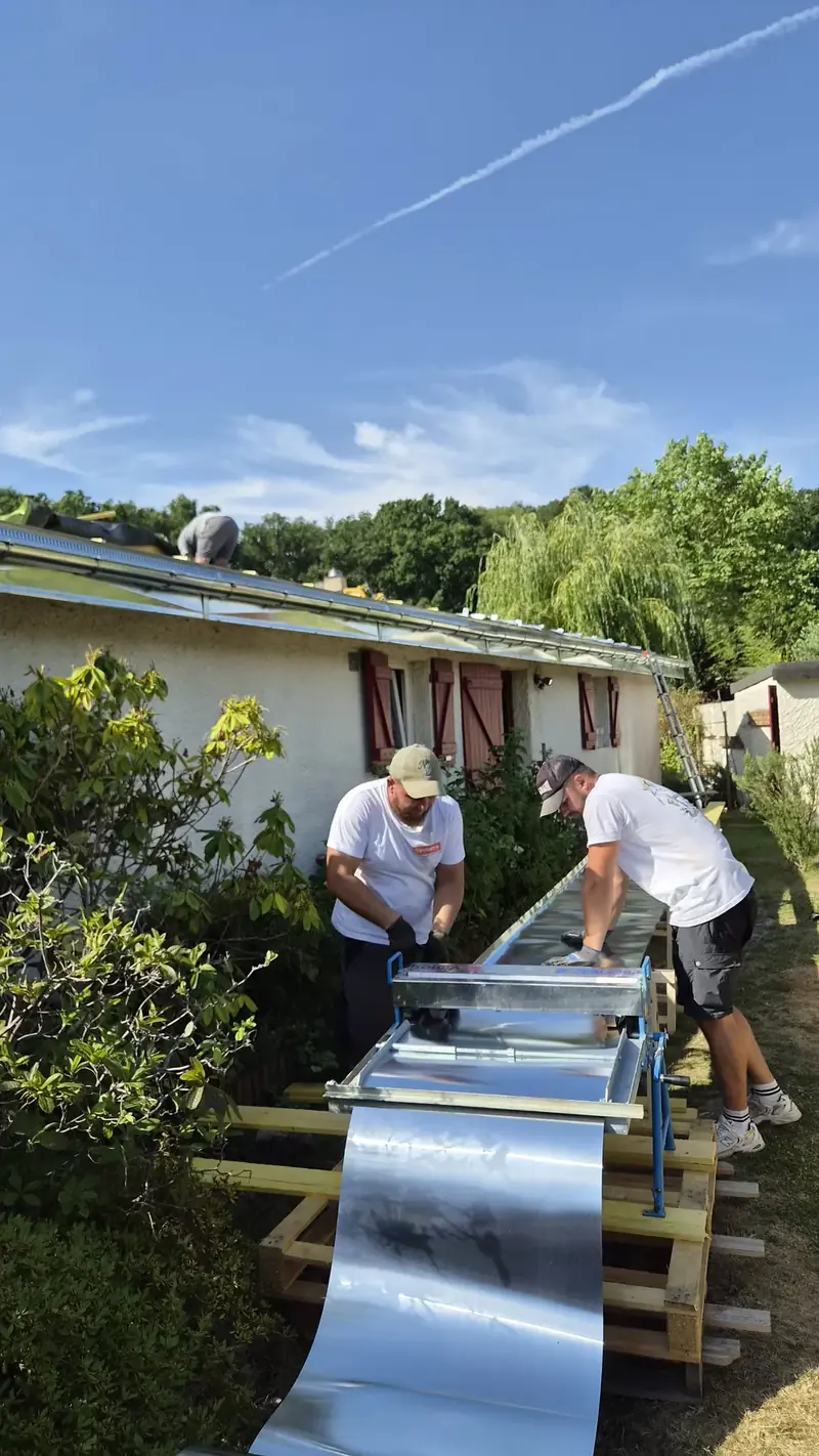 Zinc profilé sur place – Deux couvreurs profilant une bande de zinc naturel dans le jardin, au pied de la maison
